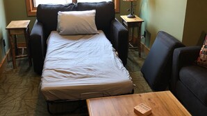 Um quarto com uma cama, dois sofás, uma mesa de madeira e uma janela com persianas.