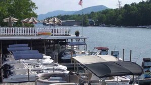 A dock with several boats, a covered area with umbrellas, and a flag. - Lake view cozy two bedroom in Bolton Landing -  walk to Town! (Bolton)