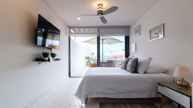 A bedroom with a bed, a ceiling fan, a TV mounted on the wall, and a view through the glass door. - Healing Roof Terrace (Playa del Carmen)