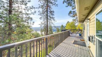 A wooden deck with a railing, overlooking a forested area and a lake.