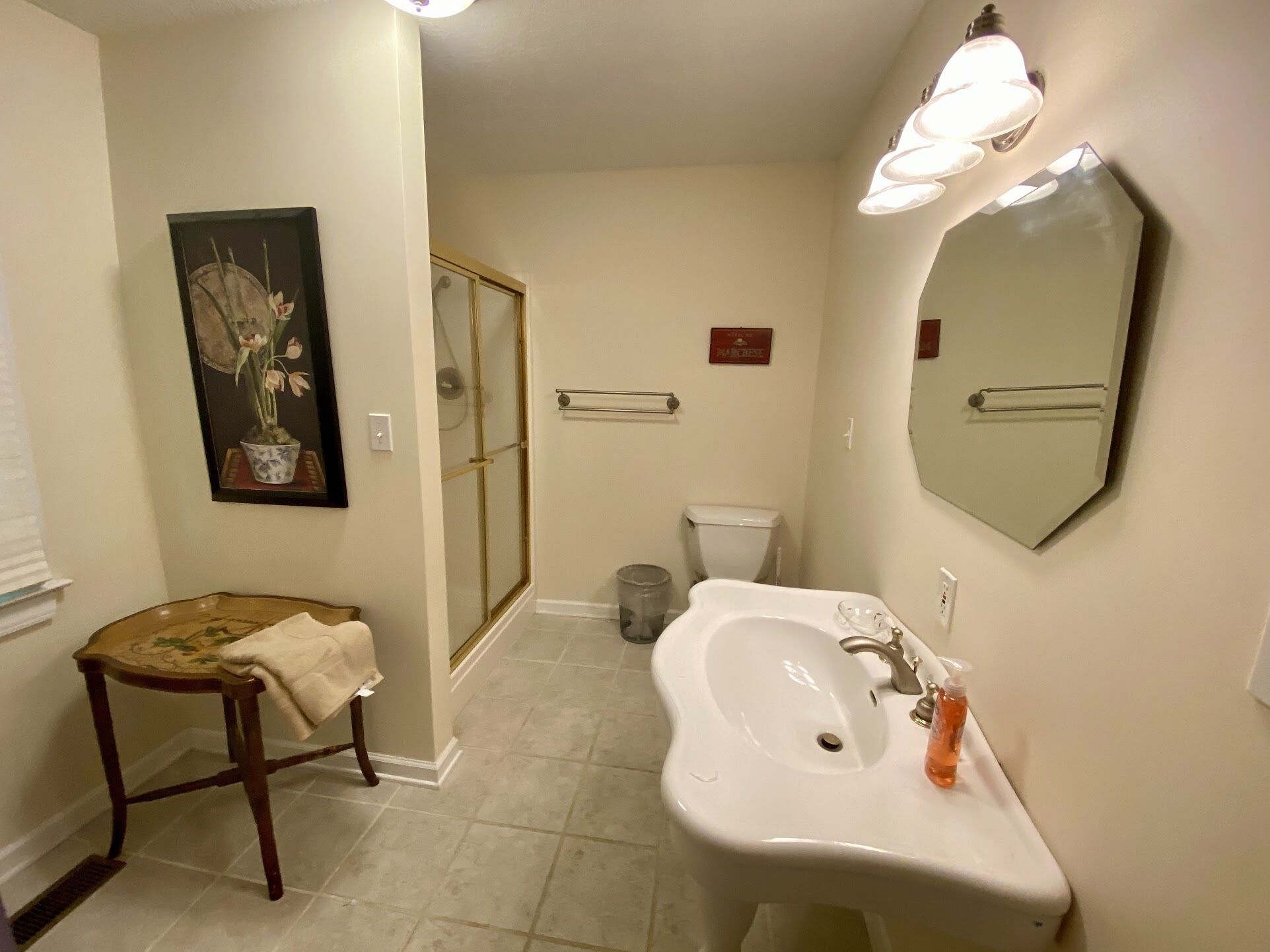 A bathroom with a sink, mirror, shower, toilet, and a small stool.