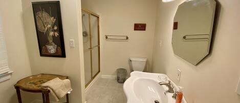 A bathroom with a sink, mirror, shower, toilet, and a small stool.