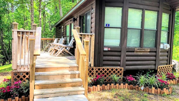 A wooden cabin with a wooden staircase leading to a deck, surrounded by a garden with various plants and flowers. - Mountain Cabin,Jacuzzi,WIFI, Pets,10min Casino/Pets (Whittier)