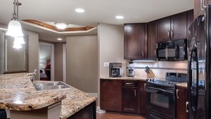 A kitchen with granite countertops, dark wooden cabinets, a stainless steel refrigerator, a black stove, and a microwave.