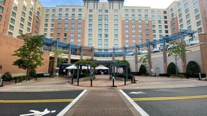 A multi-story hotel with a central courtyard, covered walkways, and a parking area with marked lanes.