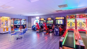 Un salón de juegos con diversas máquinas recreativas, una mesa con sillas y un letrero de neón.