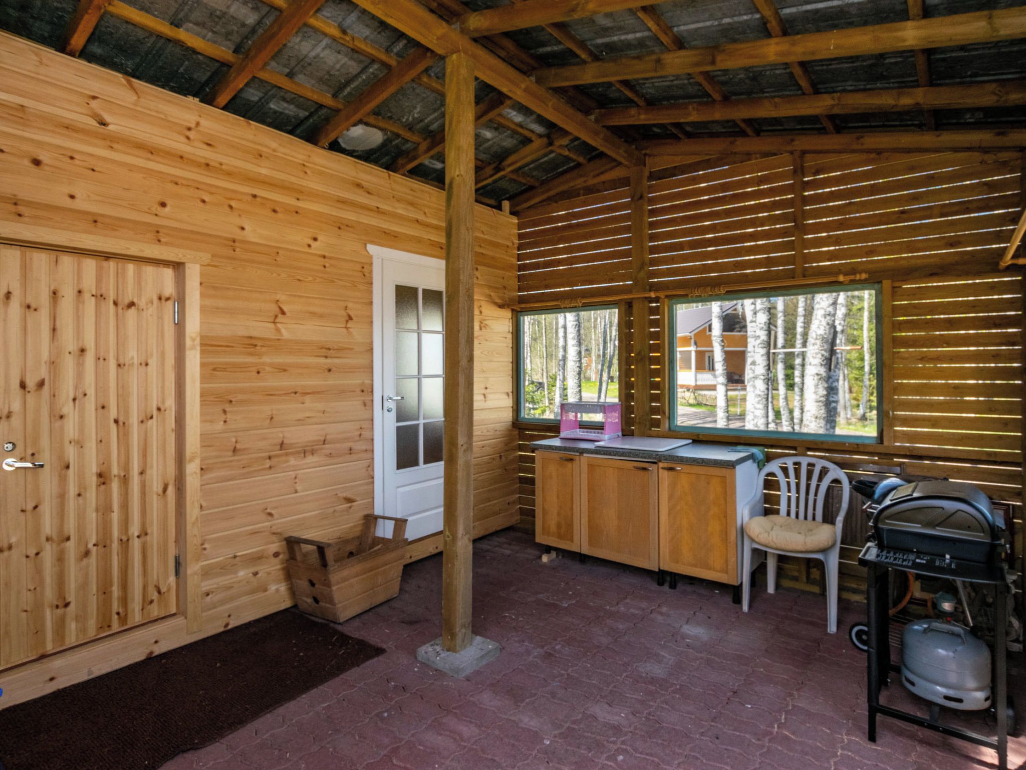 Interior de una cabaña de madera con zona de cocina, ventana con vista a árboles y estufa a gas.