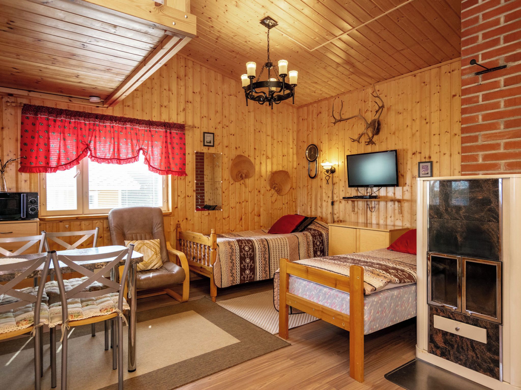 A cozy cabin interior with a wooden ceiling, a fireplace, a television, and a dining area with a table and chairs.