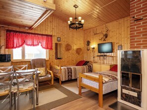 Interior acogedor de una cabaña con techo de madera, chimenea, televisor y comedor con mesa y sillas.