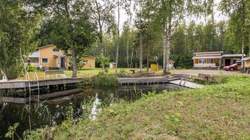 Una cabaña junto al lago con un muelle, rodeada de árboles y un pequeño estanque.