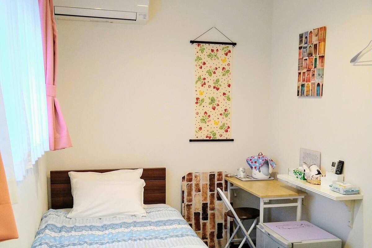 A compact hotel room with a bed, a desk, a small refrigerator, and a wall-mounted air conditioner.