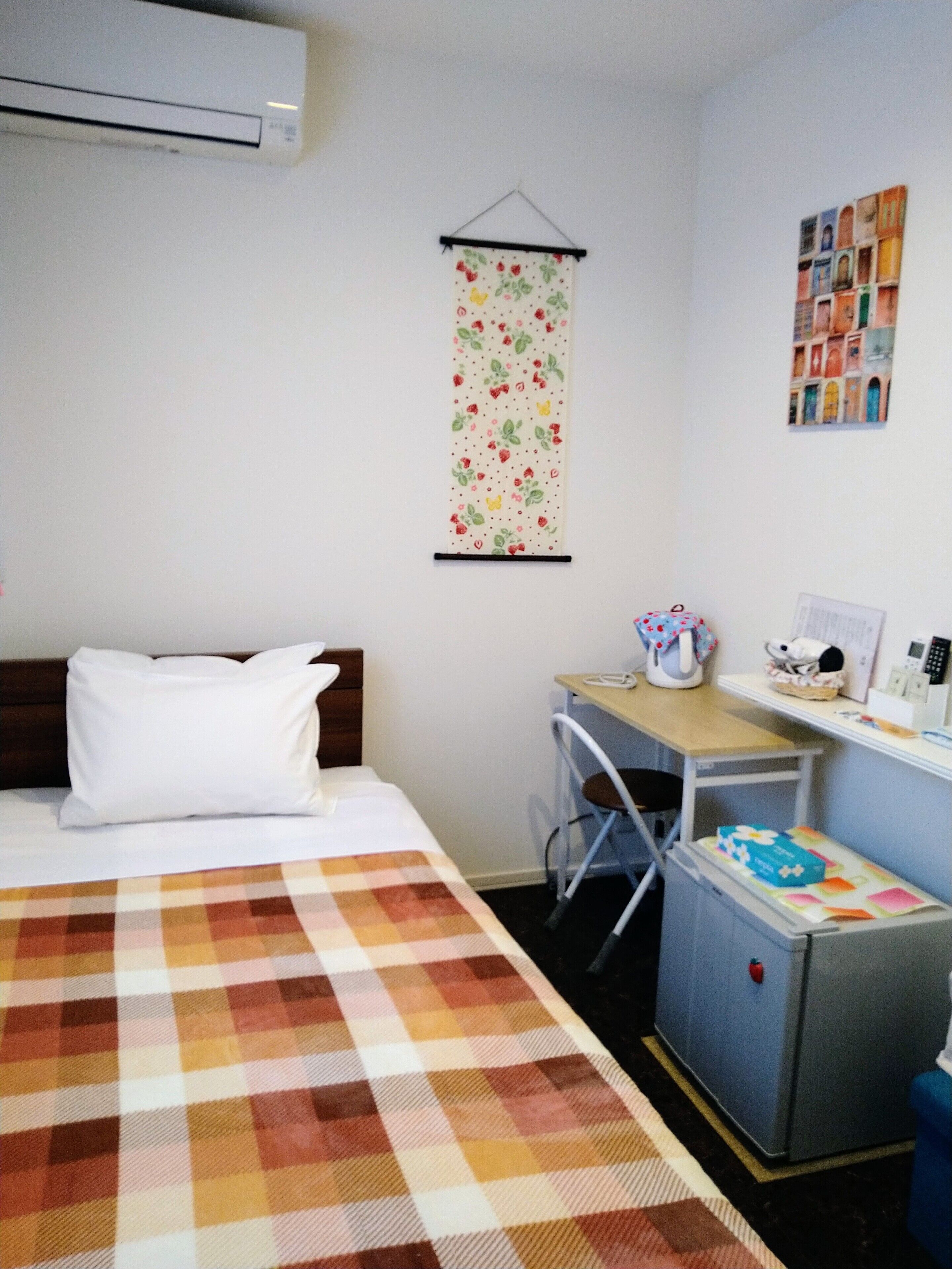 Ein kleiner, ordentlich eingerichteter Raum mit einem Bett, einem Schreibtisch, einem Stuhl und einem Kühlschrank.