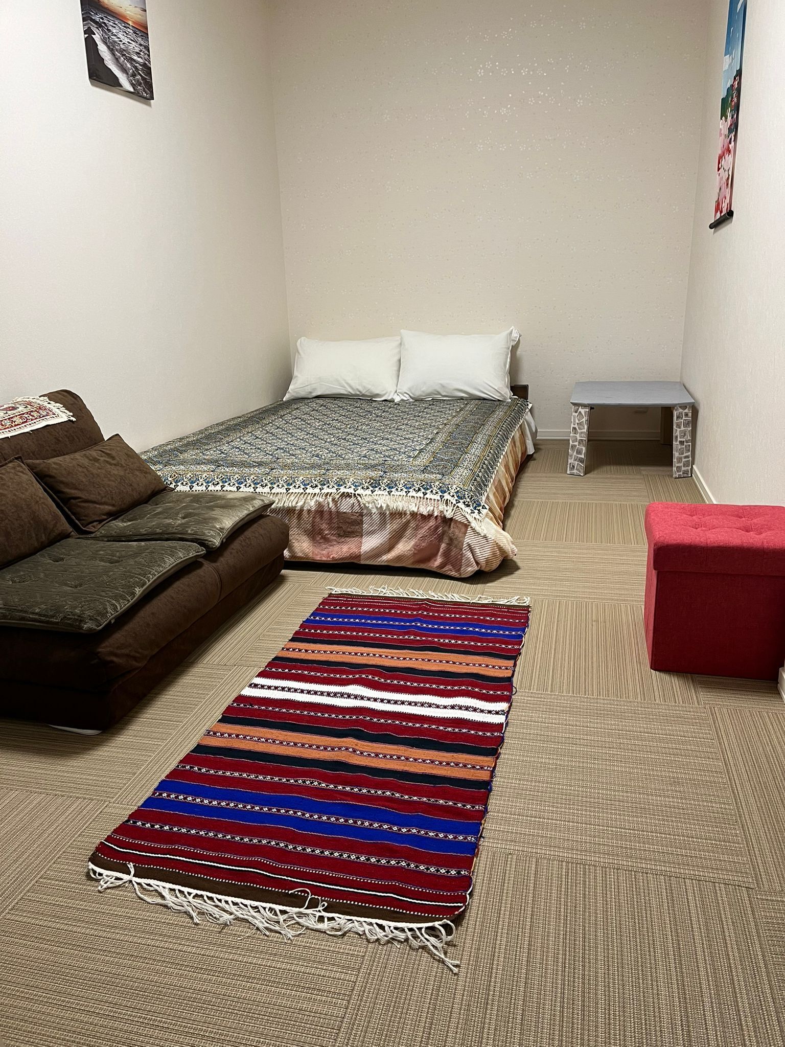 Une chambre à coucher avec un lit, un canapé, une petite table et un tapis coloré.