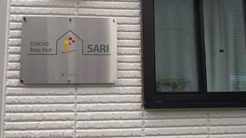 A sign for a Tokyo Stay Hut hotel with a metallic finish and a logo.
