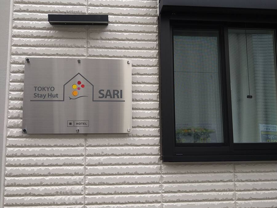 A sign for a Tokyo Stay Hut hotel with a metallic finish and a logo.