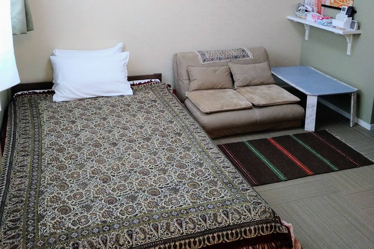 A hotel room with a large bed, a sofa, a small table, and a wall-mounted air conditioner.