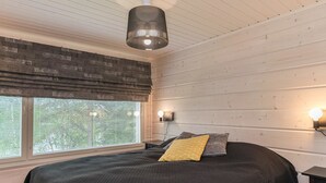 A bedroom with a large bed, a window with blinds, a hanging light fixture, and a wall-mounted light. - Valonsäde by Interhome (Valkeala)