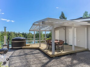 A covered outdoor deck with a table and chairs, a hot tub, and a grill. - Valonsäde by Interhome (Valkeala)