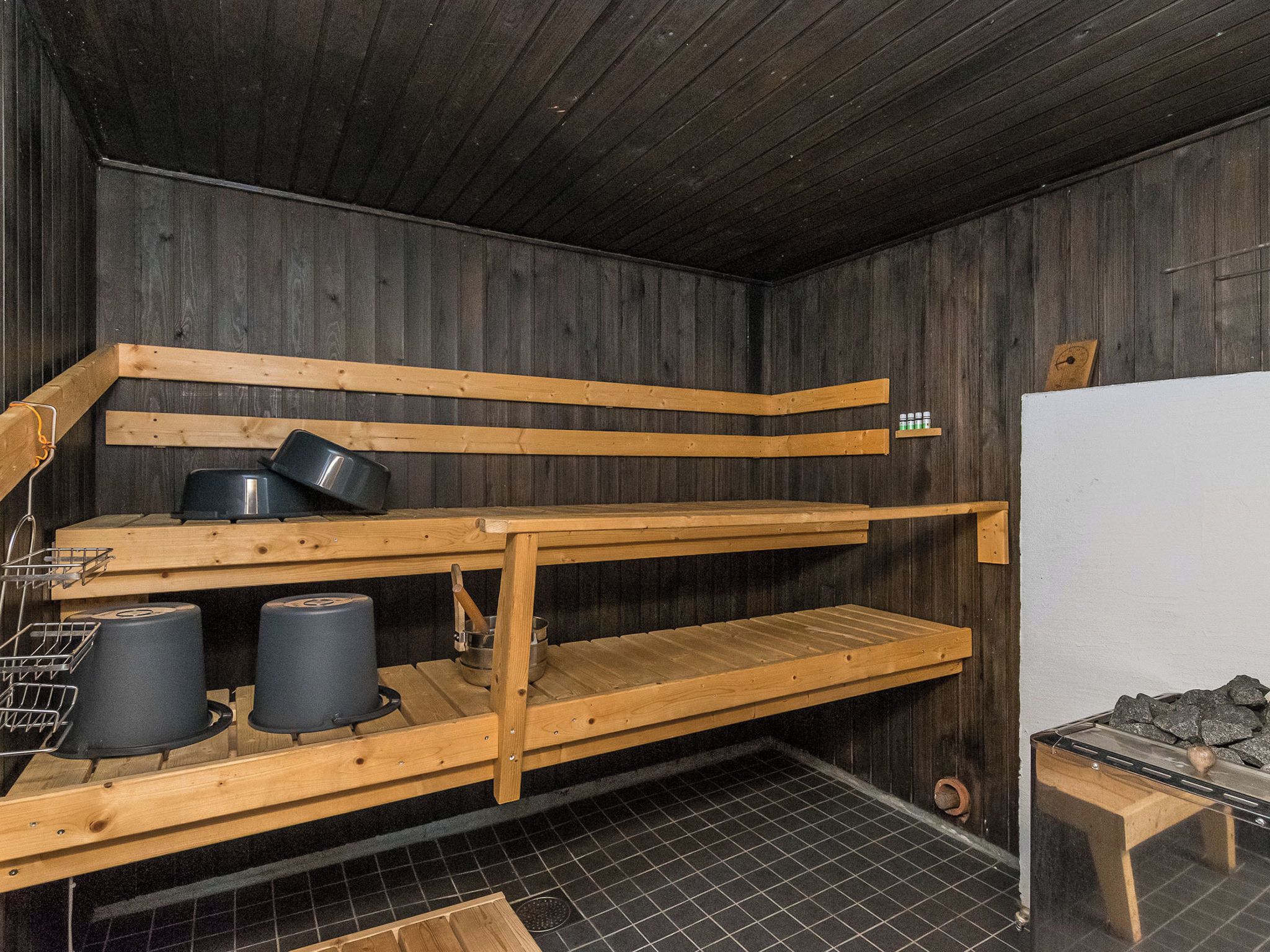 En bastu med träbänkar, ett kaklat golv och en hylla med flaskor.