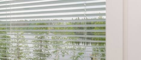 Een raam met horizontale zonwering, waardoor een uitzicht op een wateroppervlak en bomen zichtbaar is.