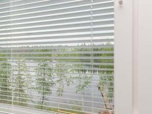 A window with horizontal blinds, through which a view of a water body and trees is visible. - Valonsäde by Interhome (Valkeala)