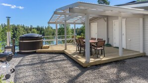 A covered outdoor deck with a grill and seating area, overlooking a lake and forest. - Valonsäde by Interhome (Valkeala)