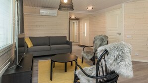 A modern living room with a grey sofa, a round coffee table, and a black wicker chair with a fur throw. There are wooden walls and a ceiling with exposed beams. - Valonsäde by Interhome (Valkeala)