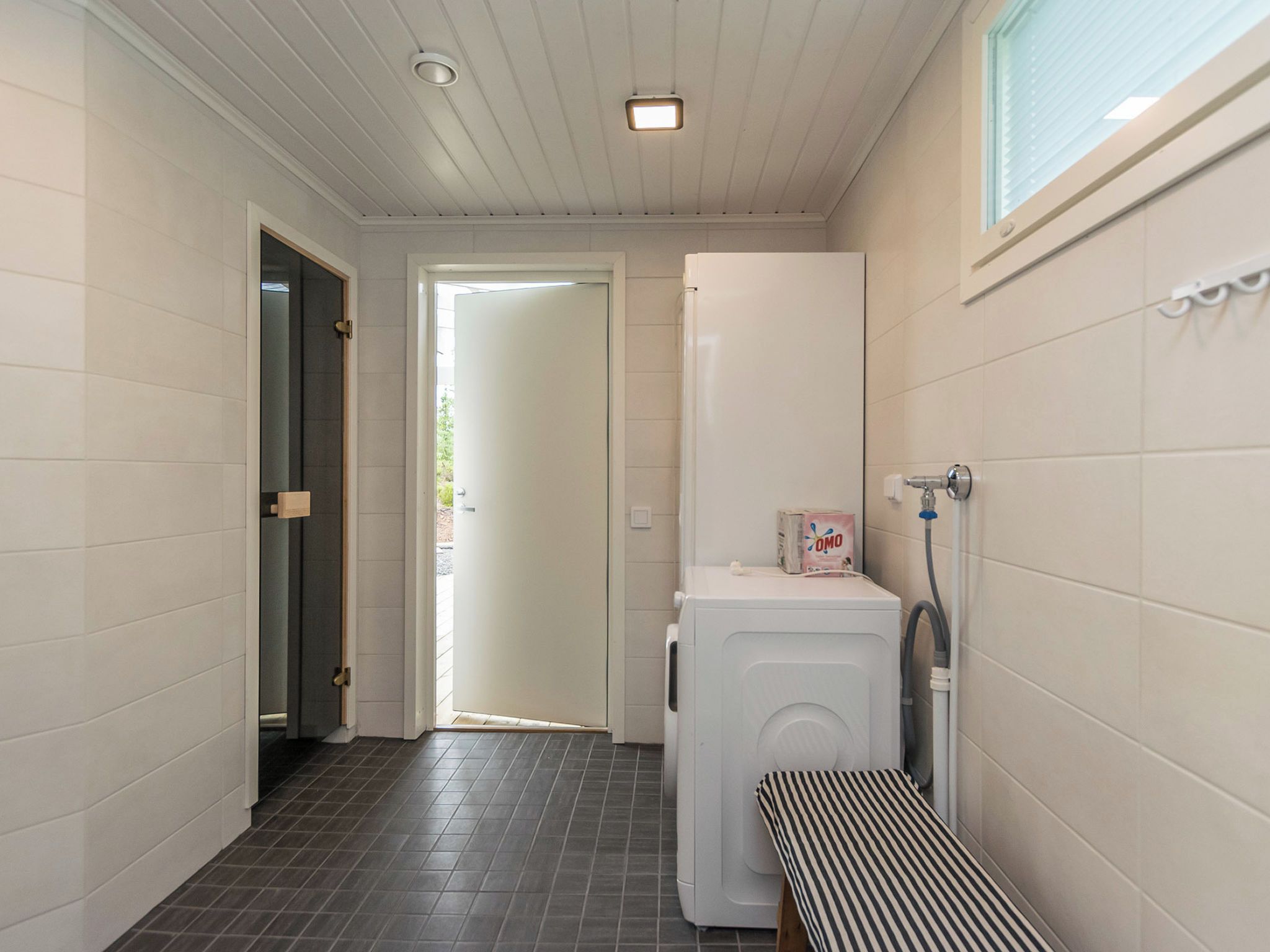 A laundry room with a washing machine, a drying rack, and a door leading to another room.