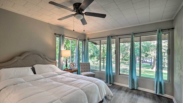 A bedroom with a large bed, a ceiling fan, and large windows with curtains. - Lake O’ the Pines Family Getaway (Avinger)