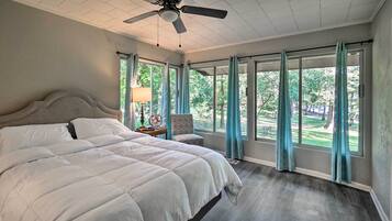 Ein Schlafzimmer mit einem großen Bett, einem Deckenventilator und großen Fenstern mit Vorhängen.