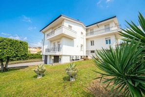 A two-story residential building with balconies, a well-maintained lawn, and two concrete planters. - Casa Michelangelo Lake Garda Terrace Apt | Sleeps 6 + AC, Desenzano Del Garda, Italy (Desenzano Del Garda)