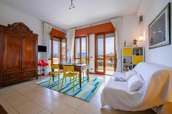 A room with a dining table, chairs, a sofa, a bookshelf, and a TV. - Casa Michelangelo Lake Garda Terrace Apt | Sleeps 6 + AC, Desenzano Del Garda, Italy (Desenzano Del Garda)