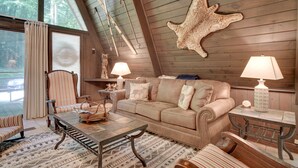 Um quarto acolhedor com teto de madeira, um tapete de pele de animal na parede, um sofá, uma mesa de centro e duas luminárias.