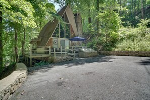 A cabin with a stone chimney, a wooden deck, and a covered seating area with a blue umbrella. - 'Snuggle Inn' in the Heart of Chalet Village! (Gatlinburg)