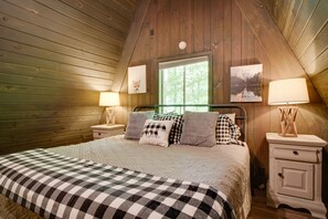 A cozy bedroom with a large bed, wooden walls, a window, and two bedside lamps. - 'Snuggle Inn' in the Heart of Chalet Village! (Gatlinburg)