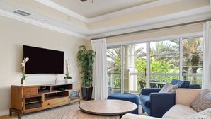 A living room with a large TV, a round coffee table, sofas, and a view of a balcony with plants. - Beautiful Condo with Private Balcony, Near Amenities (Kissimmee)