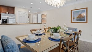 A dining area with a glass table, blue placemats, white plates, and a chandelier. - Beautiful Condo with Private Balcony, Near Amenities (Kissimmee)