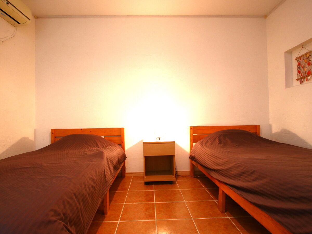 Een kleine kamer met twee eenpersoonsbedden, een nachtkastje en een luchtverkoeler aan de muur.