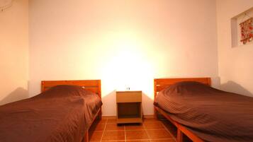 Een kleine kamer met twee eenpersoonsbedden, een nachtkastje en een luchtverkoeler aan de muur.