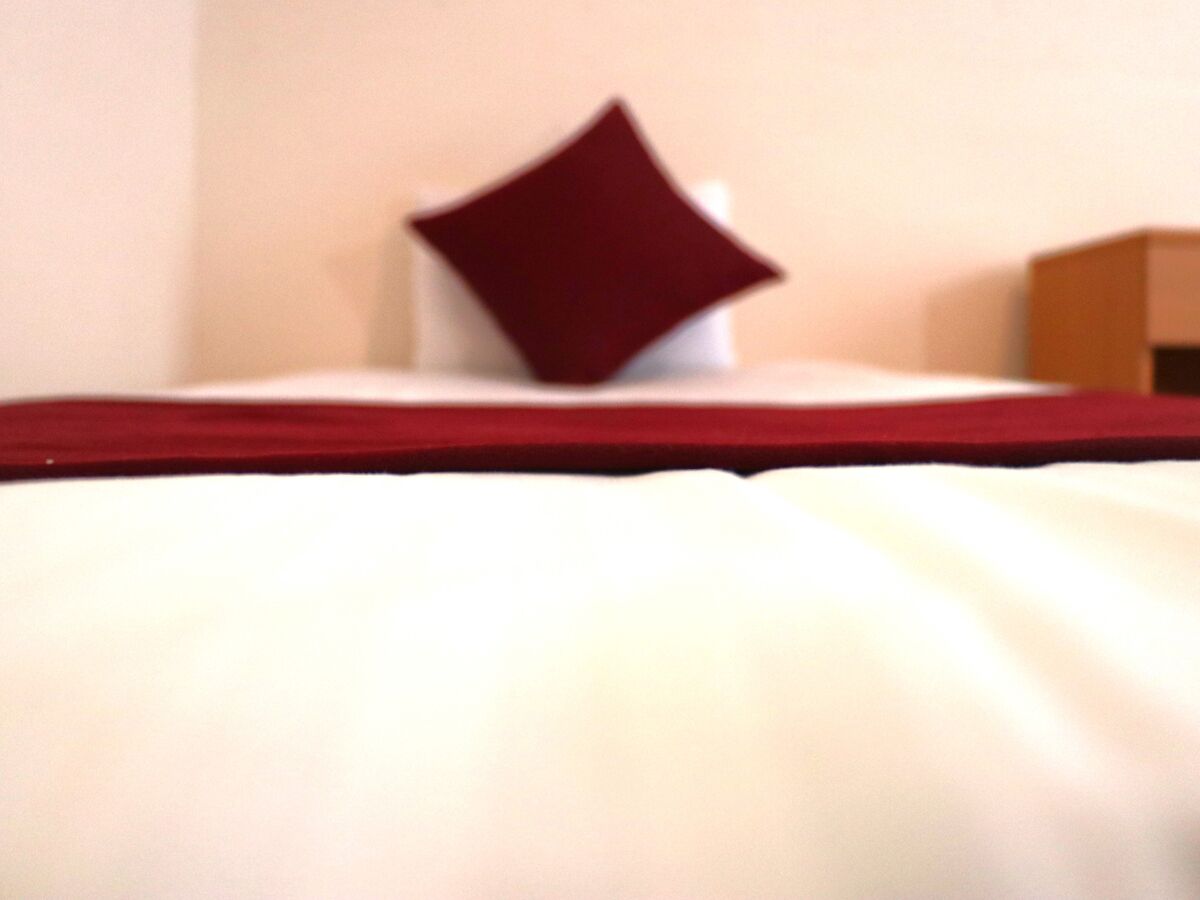 Una cama con sábana blanca y manta roja.