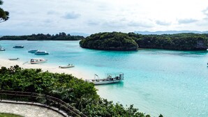 A coastal scene with boats on turquoise water, a sandy beach, and lush greenery. - Asobi Base Yamabare House Ishigakijima (Ishigaki)