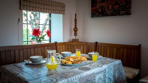 Une table à manger recouverte d’une nappe à motifs, une carafe contenant un liquide jaune, ainsi que divers plats et verres.