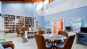 A library with bookshelves, a round table with chairs, and a computer desk with monitors. - OV 317 Golf/Pond View Condo - Paradise Vacation Rental in Ocean Village (FORT PIERCE)