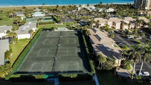 An aerial view of a coastal area with a large tennis court, beachfront properties, and a tall hotel building. - OV 317 Golf/Pond View Condo - Paradise Vacation Rental in Ocean Village (FORT PIERCE)