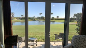 A room with a large sliding glass door leading to a patio with outdoor furniture and a view of a golf course and water feature. - OV 317 Golf/Pond View Condo - Paradise Vacation Rental in Ocean Village (FORT PIERCE)