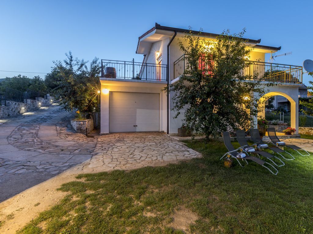 Een tweelaags huis met een garage, een balkon met een balustrade en een stenen pad dat naar de ingang leidt.