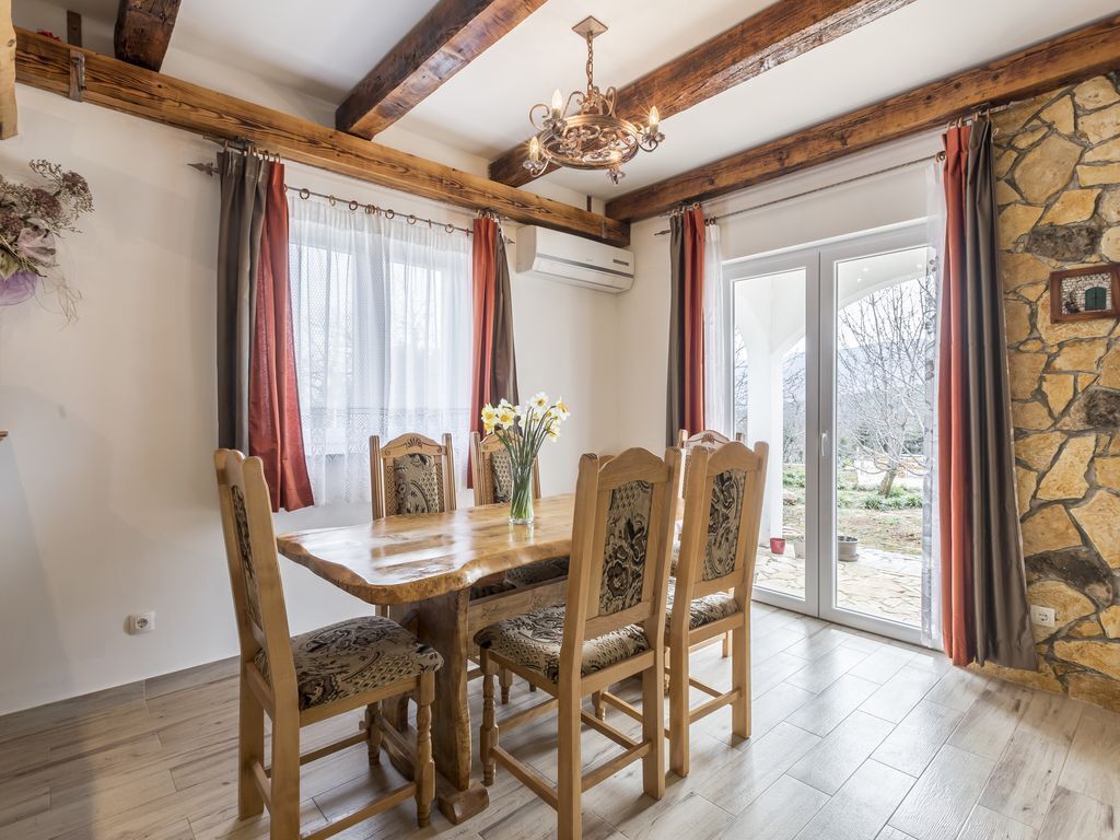 Une salle à manger avec une table et des chaises en bois, des murs en pierre et une vue sur l’extérieur.