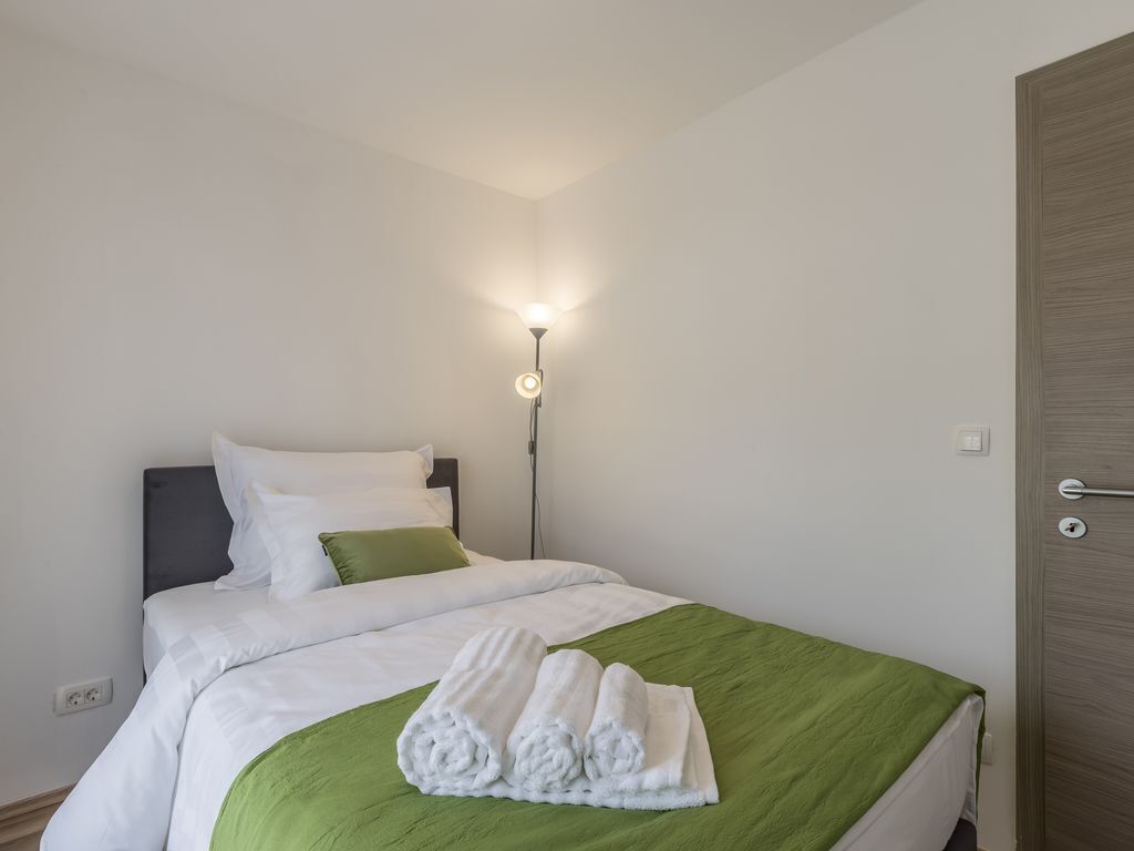 A neatly made bed with white and green bedding, a lamp on the nightstand, and a wooden door.