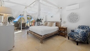 A bedroom with a canopy bed, a patterned armchair, a small bedside table, and a view of the outdoors.