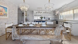 A modern kitchen with a central island, white cabinetry, and a dining area with patterned chairs and a wooden table.